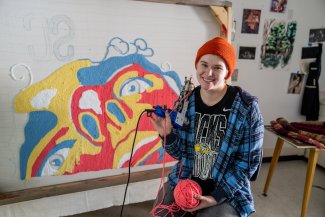 Savanna Vincent poses with an orange hat in front of colorful art