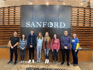 Eight chemistry club students standing by a Sanford sign.