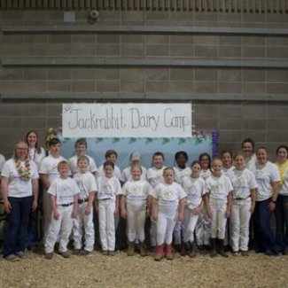 2023 Dairy camp participants in front of a Jackrabbit Dairy Camp sign in the barn.