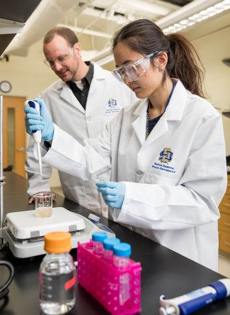 Joshua Reineke, associate professor in the Department of Pharmaceutical Sciences, assists a student working in a lab on campus.
