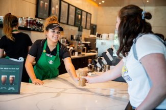A Starbucks employee handing a drink to a young woman.